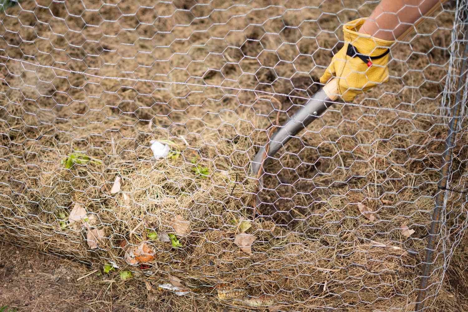 Pila de compost volteada con una pala de jardín detrás de una valla de alambre de gallinero